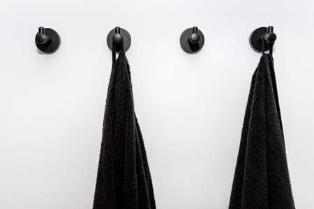 Four black towels hung on black matte hangers attached to the bathroom wall.の写真素材