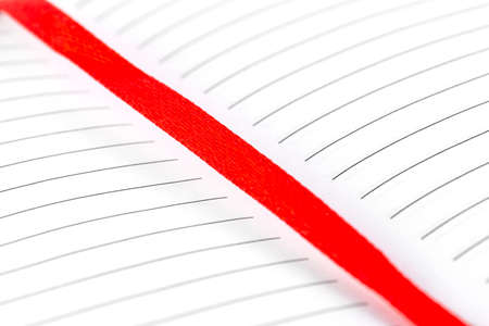 Macro photo of an open notebook with black lines and red ribbon, isolated on a white background.