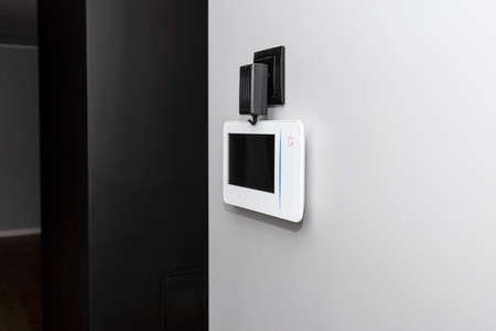 Videophone mounted on the wall with the black screen turned off, visible power supply with a cable.