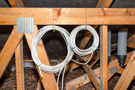 Two coils of electric cable hanging from the roof trusses in the attic of the house.