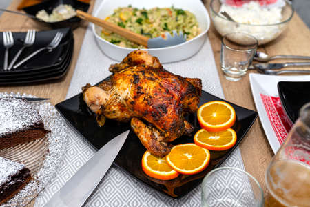 Roasted whole chicken with crispy skin lying on a black plate on a table filled with food.