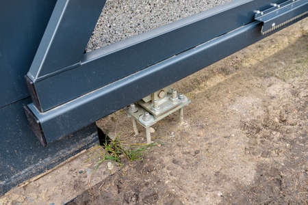 Modern sliding entrance gate in anthracite color, visible bolts attached to a concrete foundation.