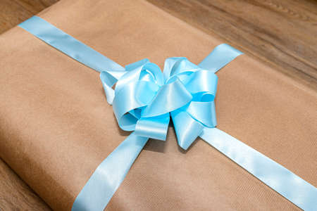 A gift wrapped in gray paper wrapped with a blue ribbon tied in a bow, lying on vinyl panels.