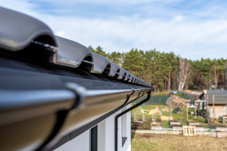 A metal, black gutter on a roof covered with ceramic tiles in the background a forest, view from...