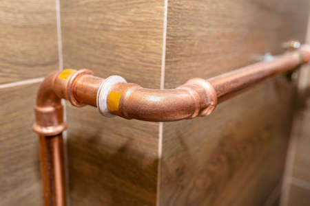 Copper pipe elbow for for natural gas installations, attached to a wall in a boiler room lined with ceramic tiles.の写真素材