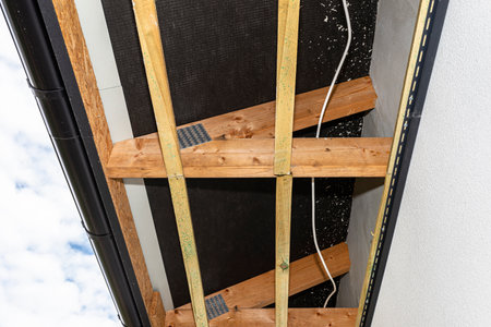 Scaffolding with three rows of wooden battens for attaching the PVC soffit, visible cables for...