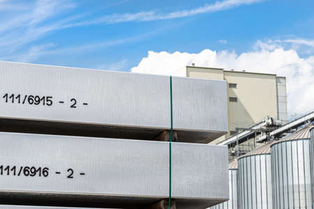 Heavy aluminum bars stacked on top of each other in an aluminum smelting plant, against the blue...