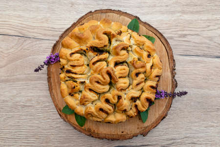 Homemade round bread with garlic butter and herbs, lying on a wooden board with basil leaves.の写真素材