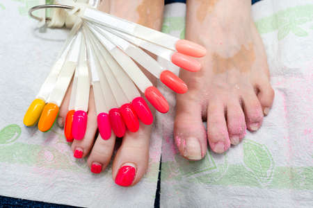 Hybrid nails painted red at the feet, a visible palette of nail colors and polished nails.の写真素材