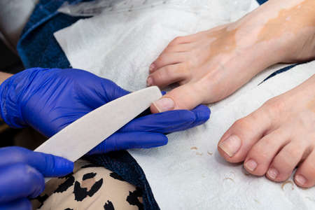The manicurist models the toenails with a nail file wearing blue latex gloves.の写真素材