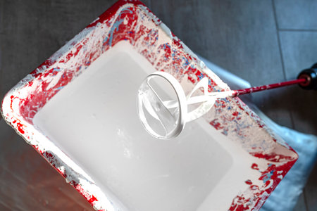 An open plastic bucket with white paint and a stirrer standing on the floor.の写真素材