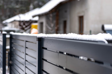 Modern anthracite panel fence with falling snow, visible sliding gate.