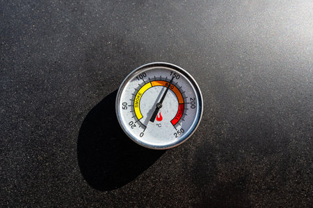 A round thermometer showing 150 degrees Celsius placed on a charcoal grill.の写真素材
