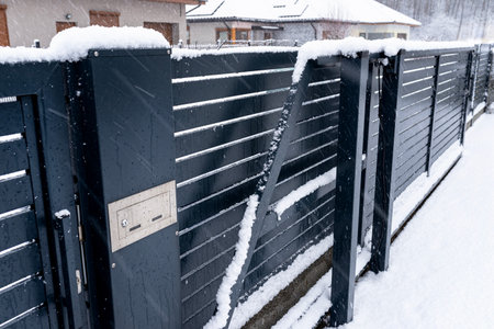A modern gate with a letterbox and a wireless card reader, mounted in an anthracite panel fence, covered with snow.の写真素材