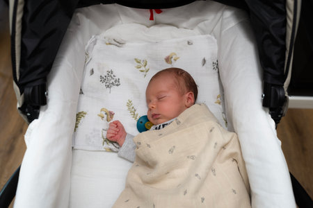 A Caucasian newborn baby sleeps on a mattress in a baby stroller.の写真素材