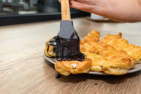 A woman spreads hot chocolate on eclairs using a silicone brush.