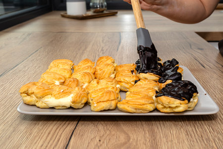 A woman spreads hot chocolate on eclairs using a silicone brush.