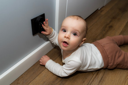 A seven-month-old baby touches a black electrical outlet on the wall.の写真素材