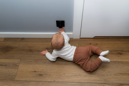 A seven-month-old Caucasian baby touches a black electrical outlet on the wall.
