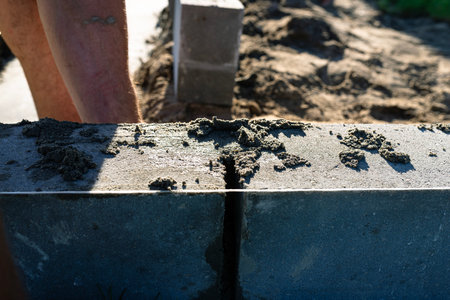A man lays concrete blocks on a poured foundation, gluing them with mortar.の写真素材