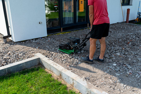 A man compacts rubble on a terrace under construction using a hand-held petrol-powered compactor.