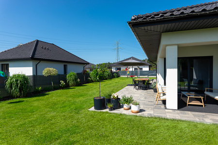 A beautiful garden with green grass, a patio table and umbrella visible, a house in beautiful summer...