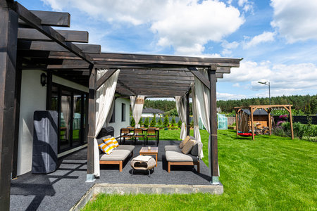The terrace behind the house is made of beams, with chairs and a table visible.