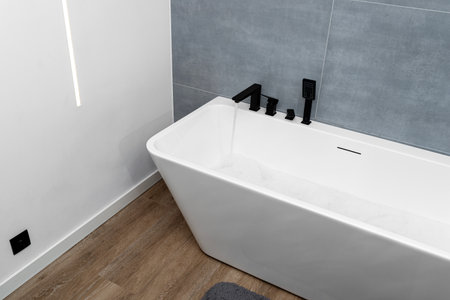 Pouring water into a modern, freestanding wall-mounted bathtub with a matte black faucet.