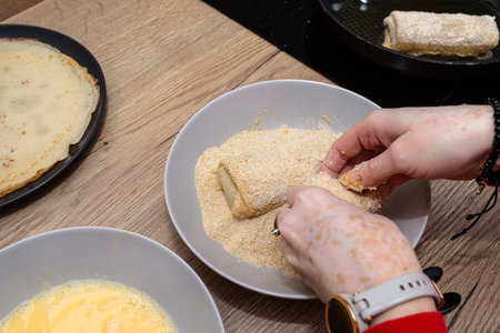 Hands breading homemade Polish croquettes with breadcrumbs and egg wash