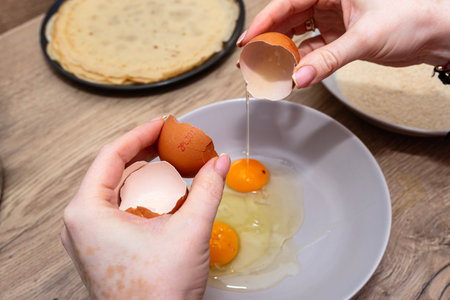 Woman's hands cracking eggs into a bowl, preparing for breading or cooking
