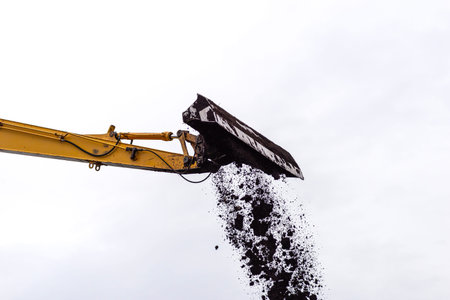 Excavator machine boom and bucket dropping soil from a construction site