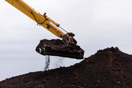 Heavy equipment excavator bucket moving soil, creating a large dirt mound