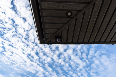 Dome security camera observing property from a ceiling against a blue sky with clouds