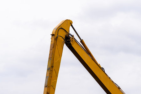 Industrial long reach excavator arm moving against a bright sky, emphasizing heavy equipment