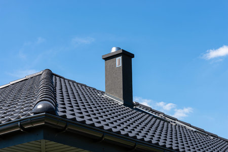 Modern dark roof with ceramic tiles, gutter, and chimney under a clear blue sky
