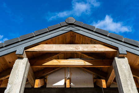 Roof structure with visible wooden trusses, concrete pillars, and dark roof tiles against blue sky