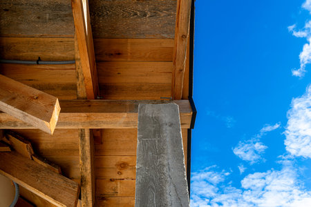 Looking up at a terrace roof structure with wooden beams and a concrete pillar under blue sky