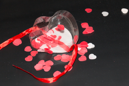 transparent heart with red ribbon and some red and white hearts in it on a black backgroundの写真素材