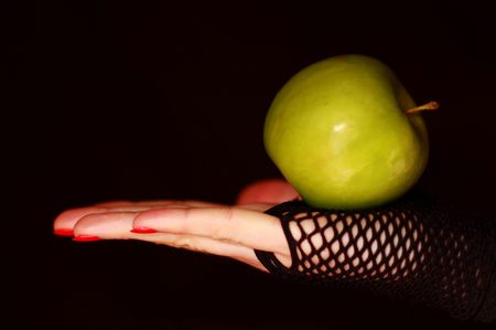 Female hand in fishnet gloves holding a green apple against black backgroundの写真素材