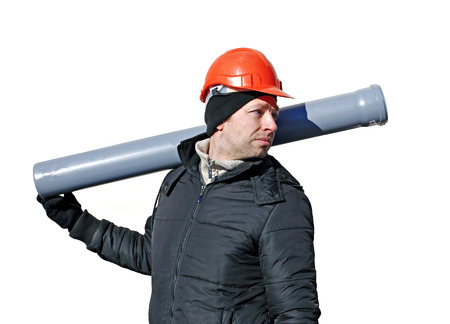 Worker at a construction site in an orange helmet with a sewer pipe in his hand isolated on white backgroundの写真素材