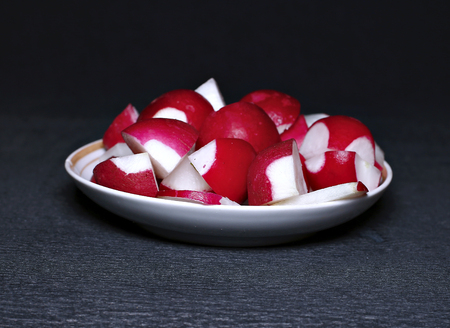Sliced red fresh radishes on a plate on a dark backgroundの写真素材
