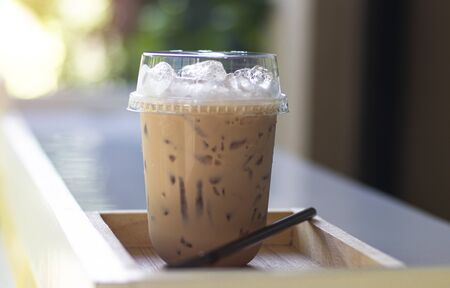 Iced milk tea in plastic glass, put on the wooden floor, behind it is a green garden.の写真素材
