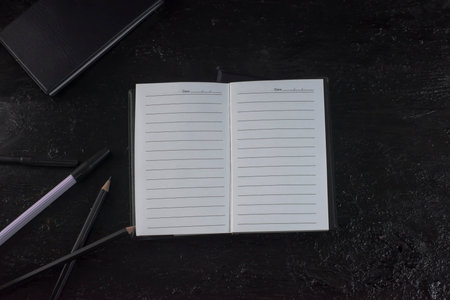 Notebook, black cover, stacked 2 books on a black background with a slight shadow. There is a black pencil on the side. and a black pen as wellの写真素材