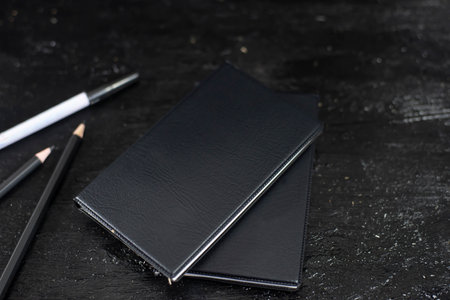 Notebook, black cover, stacked 2 books on a black background with a slight shadow. There is a black...