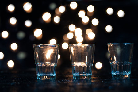 Three shot glasses lined up in a dark area with orange bogies behind them, reminiscent of the festive seasonの写真素材