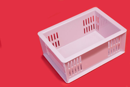 A plastic crate containing light pink items, empty, placed on a red background, waiting to be usedの写真素材