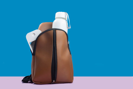 Brown shoulder bag with a water bottle and alcohol spray, ready for traveling or going to school. Bright background, blue and pinkの写真素材
