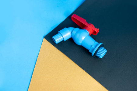 A blue plastic water tap or spigot with a red handle on a modern geometric background of blue,...