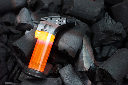 Close-up of a portable butane micro torch lighter with a bright orange fuel tank, resting on a pile...