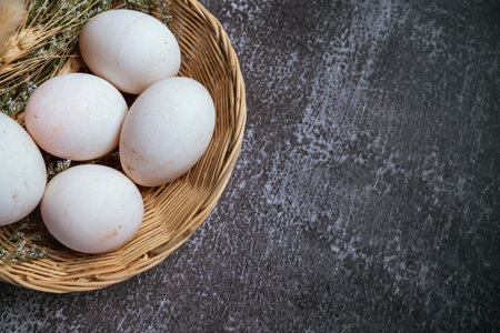 White chicken eggs in a wicker basket on black stone background.の写真素材